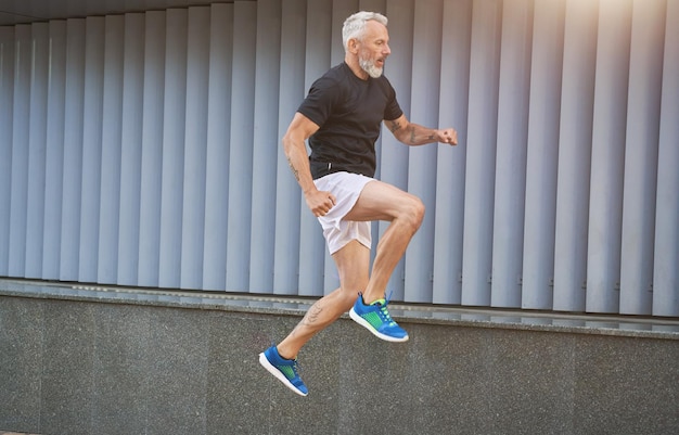 Hombre deportivo de mediana edad activo en ropa deportiva saltando y haciendo ejercicio al aire libre