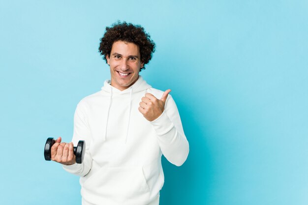 Hombre deportivo sosteniendo un dumbbel sonriendo y levantando el pulgar