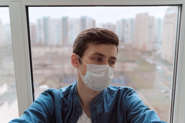 Hombre deprimido joven con máscara protectora y sentado en el balcón