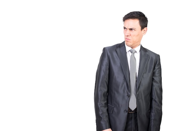 Foto hombre desagradable con cabello negro en traje formal frunciendo el ceño y sintiendo aversión mientras está de pie aislado sobre fondo blanco en estudio de luz