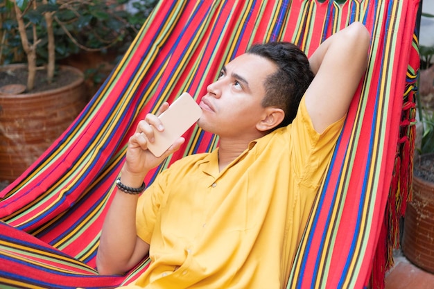 Foto hombre descansando en una hamaca en casa y usa un teléfono inteligente