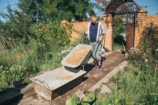 Un hombre descarga arena en una mezcla de cemento para verter un camino de jardín, trabajos de construcción en una parcela de jardín