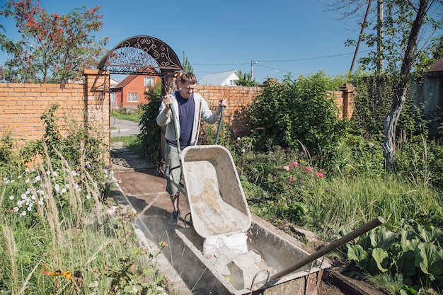 Un hombre descarga arena en una mezcla de cemento para verter un camino de jardín, trabajos de construcción en una parcela de jardín