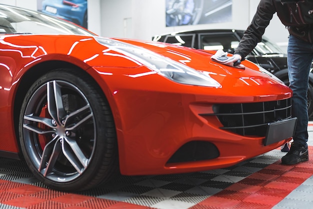 Hombre desconocido puliendo un coche naranja con un taller de reparación de telas