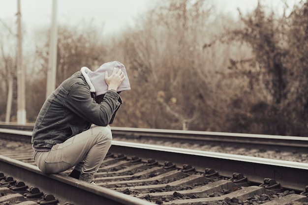 Hombre desesperado sentado en el ferrocarril Vista lateral de un hombre desesperado con ropa informal tocando la cabeza mientras se sienta sobre rieles en el campo de otoño