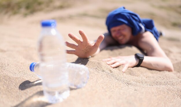 Foto hombre deshidratado arrastrándose por la arena por una botella de agua potable de cerca