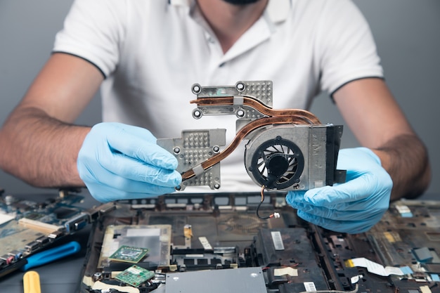 Foto un hombre desmonta una computadora portátil en una pared gris