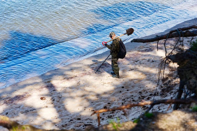 Un hombre con un detector de metales camina al borde del agua de una playa de arena