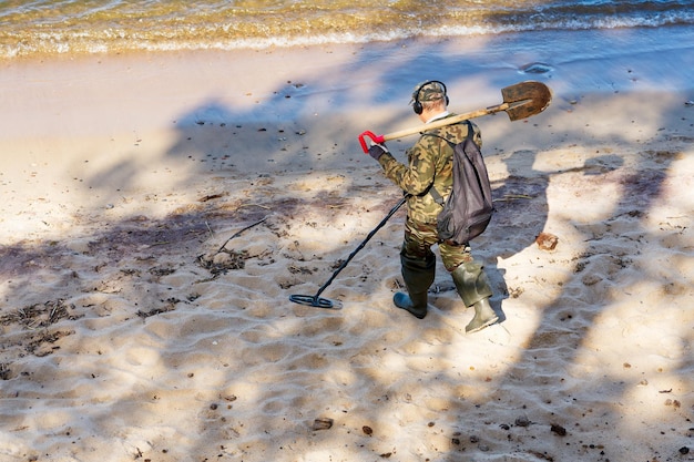 Un hombre con un detector de metales camina al borde del agua de una playa de arena