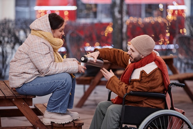 Hombre con discapacidad compartiendo bebidas calientes con una mujer joven en una cita en la ciudad de invierno