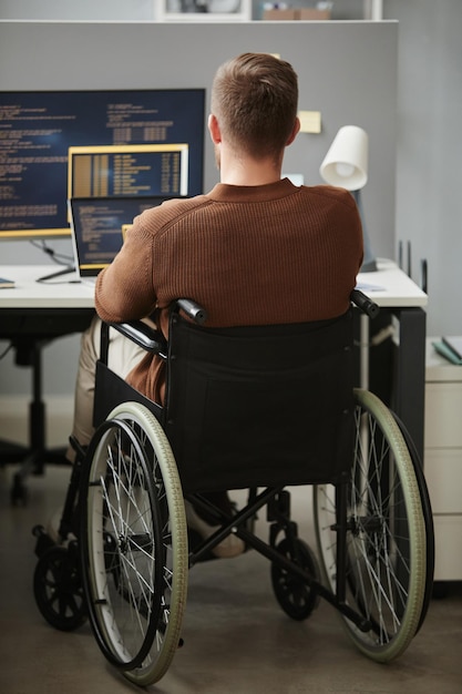 Hombre con discapacidad escribiendo código trabajando en un escritorio en un cubículo de oficina