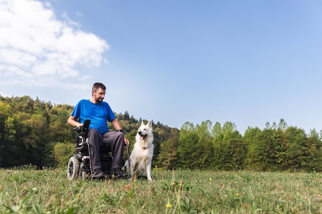 Hombre con discapacidad física en una silla de ruedas y su mejor amigo un hermoso perro blanco disfrutando de una