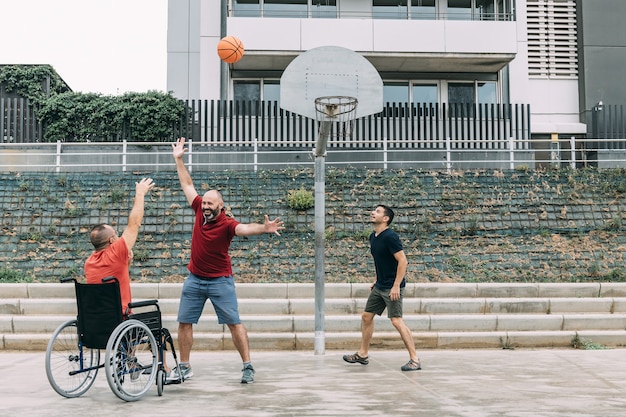 Hombre discapacitado jugando baloncesto con dos amigos