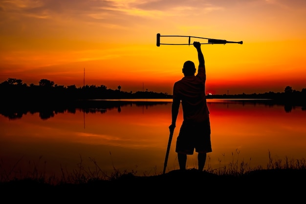 Foto hombre discapacitado con muletas en el fondo del amanecer.