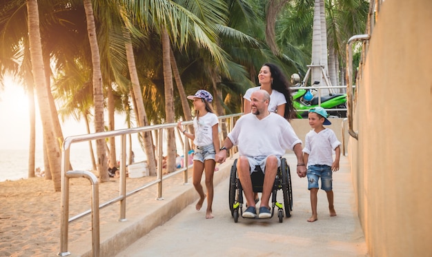 Hombre discapacitado en silla de ruedas se mueve en una rampa a la playa con su familia.