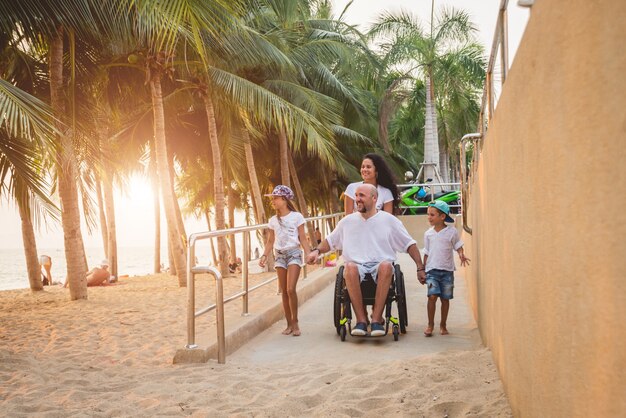 Hombre discapacitado en silla de ruedas se mueve en una rampa a la playa con su familia.