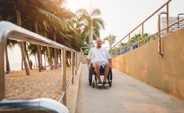 Hombre discapacitado en silla de ruedas se mueve en una rampa a la playa.