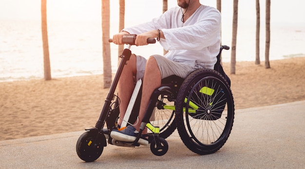 Hombre discapacitado en silla de ruedas con scooter eléctrico en la playa.
