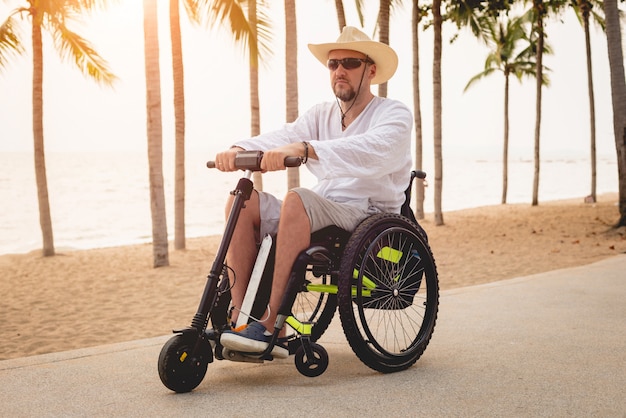 Hombre discapacitado en silla de ruedas con scooter eléctrico en la playa.