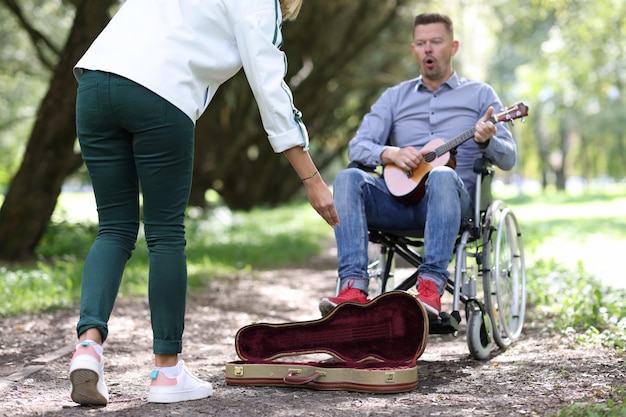 Hombre discapacitado en silla de ruedas toca la guitarra en el parque y gana dinero músico callejero discapacitado