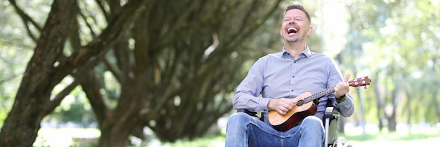 Hombre discapacitado en silla de ruedas toca la guitarra en el parque y gana dinero músico callejero discapacitado