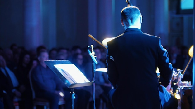 Un hombre disfrazado tocando la batería y mirando notas en el concierto de jazz Vista posterior