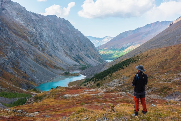 El hombre disfruta de la hermosa vista del lago alpino azul en el colorido valle de otoño El turista disfruta del lago de montaña azul La vista panorámica de la colina roja entre la flora multicolor Los colores vívidos del otoño en las altas montañas