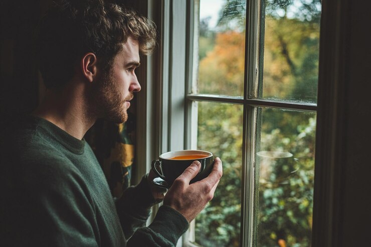 Hombre disfrutando de una bebida caliente mientras mira por una ventana acogedora en otoño IA generativa