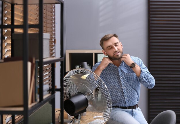 Hombre disfrutando del flujo de aire del ventilador en el lugar de trabajo