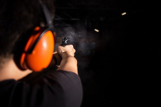 Foto el hombre dispara una pistola de pistola, dispara una bala y usa una cubierta de oreja naranja en el campo de tiro