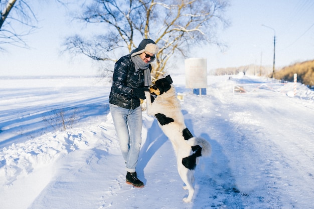 Hombre divertido bailando con perro en frío día de invierno en la naturaleza.