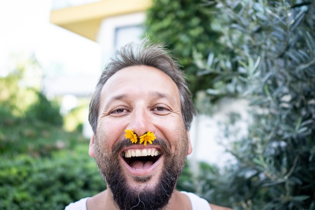 Hombre divertido con flor en la nariz riendo en el jardín