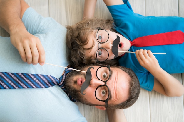 Hombre divertido y niño con bigote falso. Familia feliz, juego, en casa