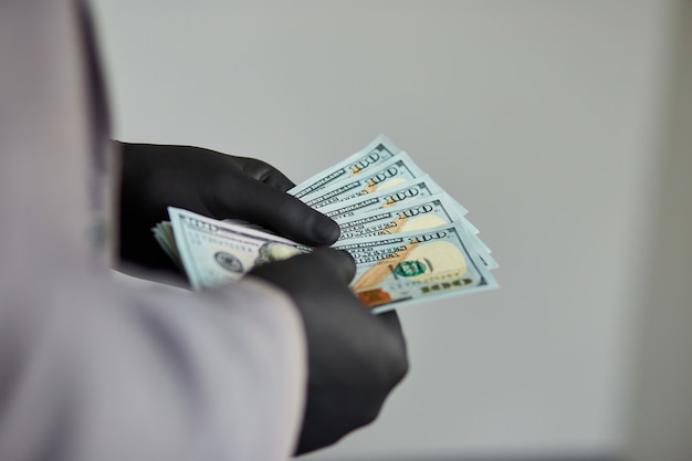 Hombre con dólares de dinero en la mano en guantes médicos negros. Ahorrar dinero.