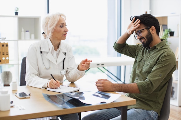 Foto hombre con dolor de cabeza escuchando recomendaciones con respecto al historial médico