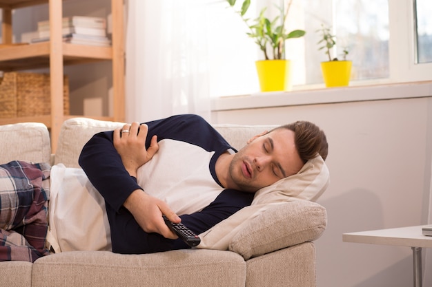 Hombre dormido en casa mientras ve la televisión.