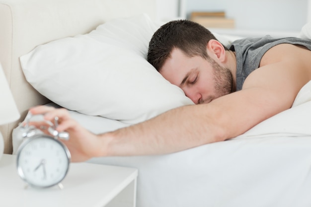 Hombre dormido siendo despertado por un reloj despertador