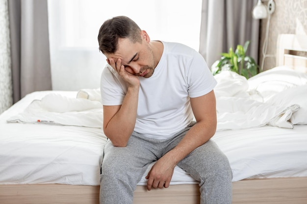 Un hombre sin dormir se sienta en una cama en el dormitorio por la mañana.