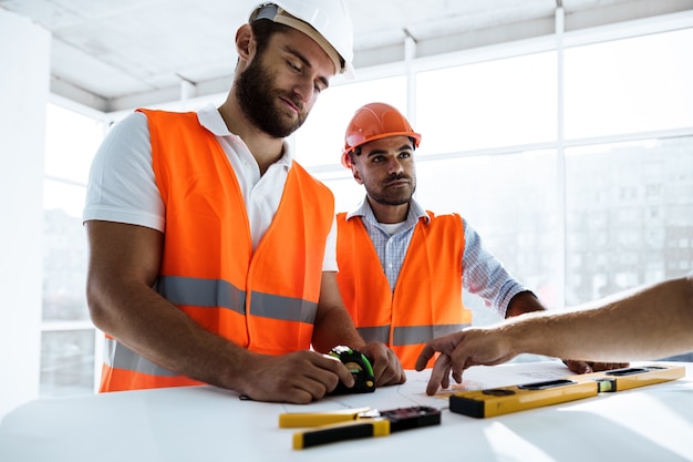 Hombre de dos ingenieros mirando el plan del proyecto sobre la mesa en el sitio de construcción