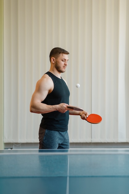 Hombre con dos raquetas golpea ping pong en interiores.