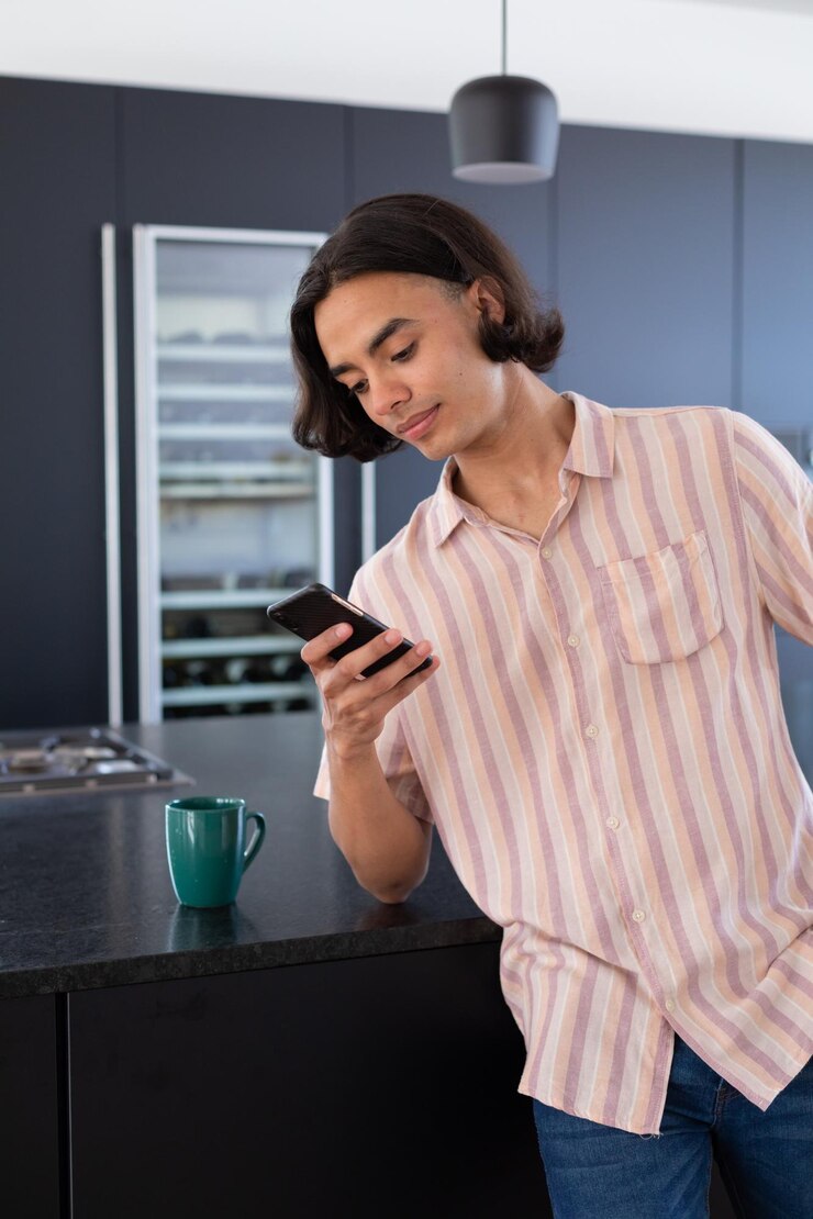 Foto hombre de dos razas feliz usando un teléfono inteligente en la cocina, pasando tiempo de calidad en casa solo, la vida doméstica y el concepto de estilo de vida.
