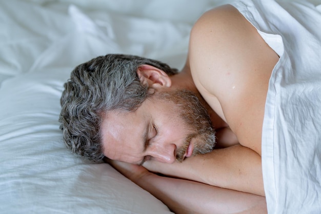 El hombre duerme en la cama blanca el hombre sexy sin camisa duerma en la cama en el dormitorio el hombre maduro hispano duerme En casa