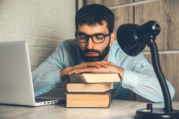 Hombre durmiendo en el libro con la computadora en el escritorio