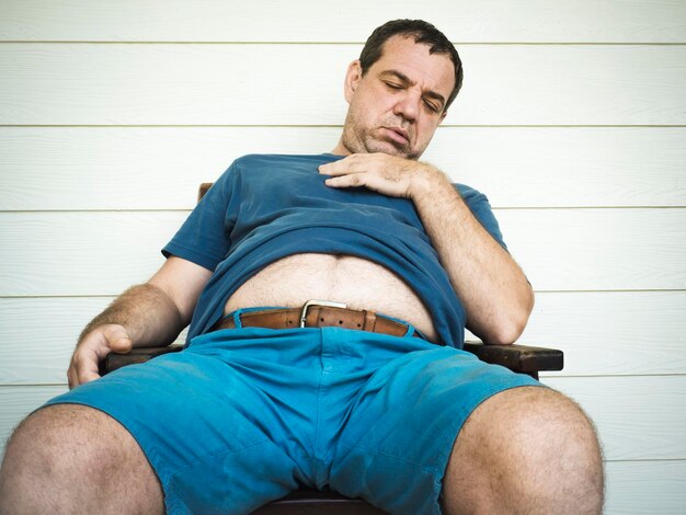 Foto hombre durmiendo sentado en una silla contra la pared