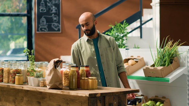 Hombre eco-consciente comprando alimentos frescos en una tienda de comestibles local con productos de cultivo casero en busca de productos químicos y aditivos libres persona de Oriente Medio examinando estantes con especias