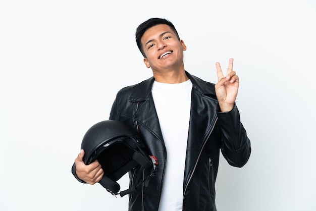 Hombre ecuatoriano con un casco de motocicleta aislado sobre fondo blanco sonriendo y mostrando el signo de la victoria