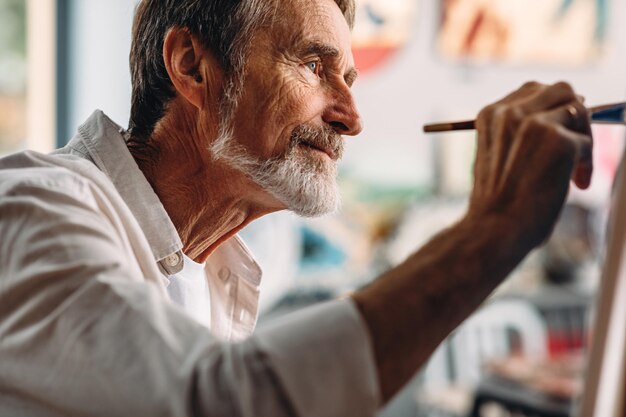 Foto hombre de edad avanzada con pintura con pincel en el taller