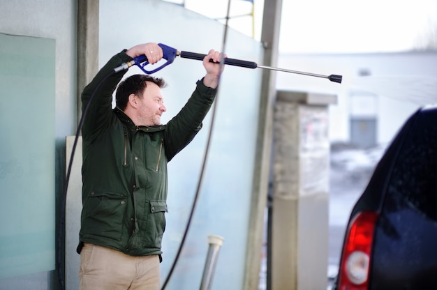 Hombre de la Edad Media que lava un coche en un carwash. Auto limpio