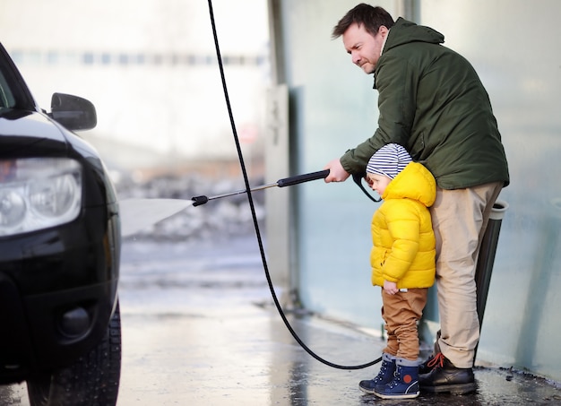 Hombre de la edad media y su pequeño hijo que lavan un coche en un lavado de autos. Tiempo familiar