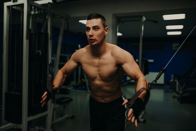 Un hombre ejerciendo trx de entrenamiento de suspensión en el gimnasio oscuro